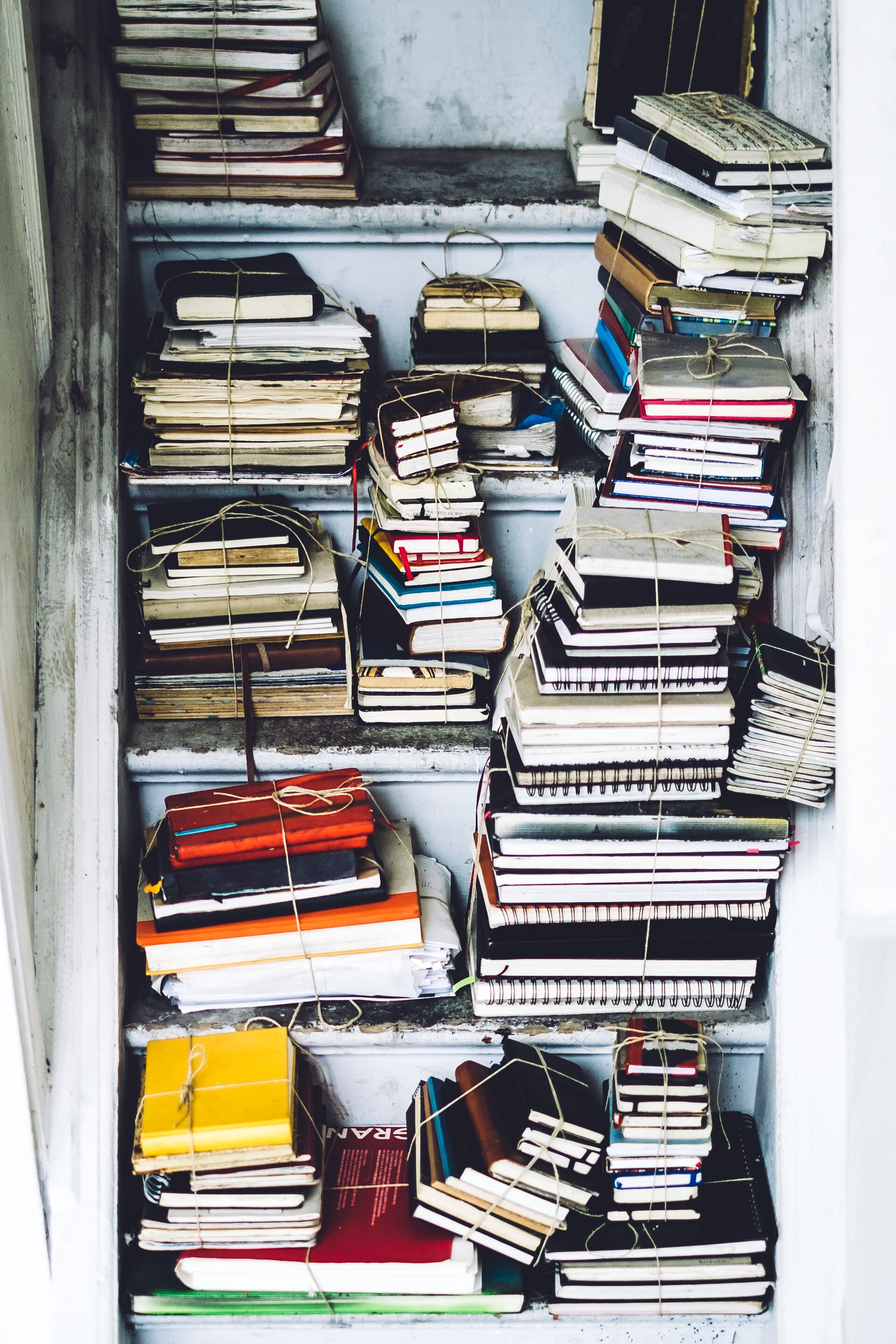Des piles de vieux carnets ficelés rangés sur des étagères blanches — raconter au passé en français